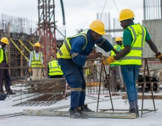 A diverse group of construction workers in safety gear at an active building site.