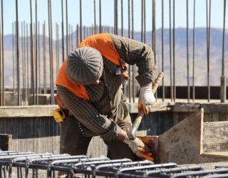 A construction worker in safety gear working at a sunlit site with mountains in background.
