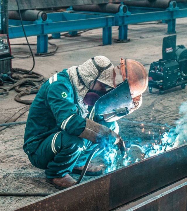 A welder using protective gear works on metal in a factory workshop.
