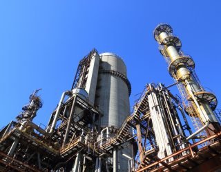 A towering industrial plant under a vivid blue sky, showcasing its intricate architecture and industrial prowess.