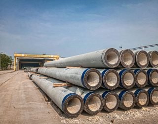 Stacked industrial concrete pipes near a construction area under clear skies.